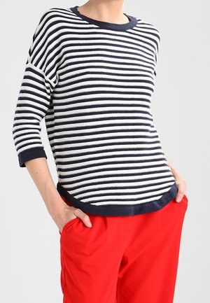 Maglia a righe a maniche lunghe blu navy e bianca, con scollo rotondo e bordi blu navy a contrasto, abbinata a pantaloni rossi.