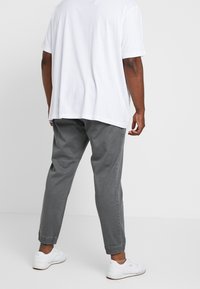 Harmaat kapealahkeiset puuvillahousut, joissa on joustavat resorit lahkeissa. Yhdistetty löysään valkoiseen t-paitaan ja valkoisiin lenkkareihin. Yksinkertainen muotoilu ja rento istuvuus.