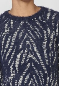 Suéter azul marino con un patrón en zigzag de color gris claro, hecho de una textura esponjosa, con un escote ancho y un tejido de punto suave.