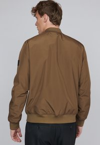 Brown bomber jacket with a smooth, shiny finish, ribbed cuffs, and hem. Features a stand collar and a black accent on the sleeve.