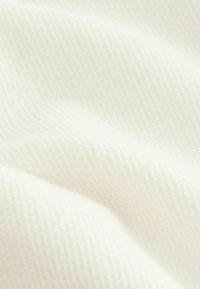 Tissu blanc texturé avec un motif à fines côtes, doux au toucher, affichant de douces courbes et plis dans le matériau.