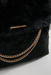 Czarna torebka z futra syntetycznego z złotymi akcentami �łańcuszka, o prostokątnym kształcie i subtelną plakietką z logo. Miękka faktura i elegancki design.
