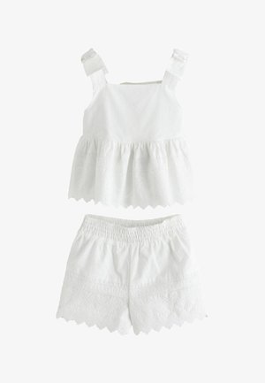 Biely nátelník bez rukávov s volánovým lemom a vyšívané šortky s oblými okrajmi, obidva vyrobené z ľahkej látky s dierkovaným vzorom.