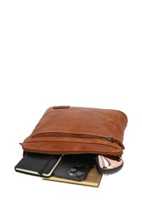 Hnědá kožená taška na notebook se zipovým uzávěrem. Obsahuje notebook, chytrý telefon a kosmetickou paletu, přičemž všechny jsou částečně viditelné uvnitř.