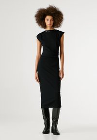 Abito nero midi con forma aderente, maniche corte, tessuto testurizzato e accenti metallici decorativi attorno al colletto; abbinato a stivali neri sopra il ginocchio.