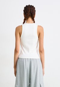 Hvid stribet tanktop med rund udskæring og smalle stropper, parret med grå shorts med elastik i taljen og sidelommer.