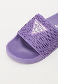 Sandal in plastica viola con una fascia testurizzata decorata con piccole borchie e un patch a forma triagolare. Soletta liscia e materiale resistente.