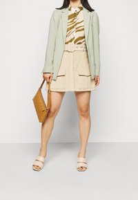 Ljusgrön blazer, mönstrad skjorta med beige och olivgröna ränder, beige kjol med fickor, tan kviltad handväska och ljusrosa sandaler.