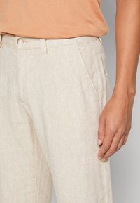 Beiga byxor i fiskbensmönster med en slät textur, med framfickor, knappstängning och rak benform.