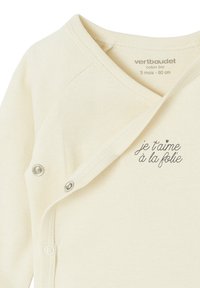 Cremfarbener Baby-Wickelshirt aus Bio-Baumwolle mit Druckknöpfen und gesticktem französischen Text "je t'aime à la folie" in der Nähe des Halsausschnitts.