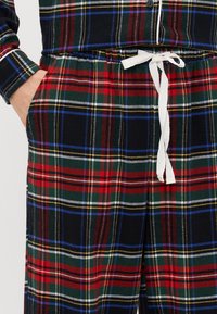 Rutet pyjamasæt med sort bund og røde, grønne, blå og gule striber, blødt stof, elastisk talje og hvid snor.