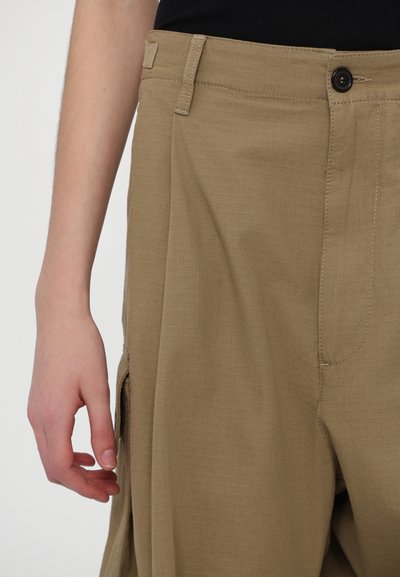 Beige cargo püksid tekstuuriga kangast, millel on nuppude sulgemine, küljetaskud ja mugav lõige. Detailne õmblemine on nähtav.