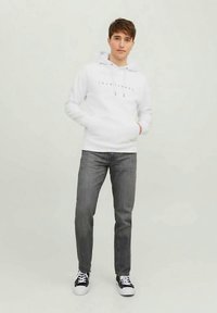 Felpa bianca con coulisse e testo stampato, abbinata a jeans grigi e sneakers nere. Design semplice, stile casual, accenti minimi.