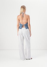 Denim halterneck-top dengan punggung terbuka, diikat di leher, dipadukan dengan celana lebar bergaris putih, menciptakan siluet yang santai.