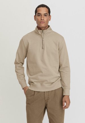 Felpa beige con zip e colletto alto, realizzata in tessuto morbido. Presenta polsini e orlo a costine, design minimalista e vestibilità rilassata.