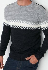 Pull en tricot avec un design en blocs de couleurs gris, blanc et noir. Motifs texturés avec des éléments ondulés et en zigzag, col rond et poignets côtelés.