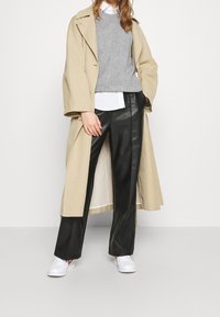 Trench coat beige, maglione grigio, camicia bianca con colletto, pantaloni di pelle neri e sneaker bianche con dettagli rossi. Texture morbide e design su misura.