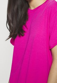 T-shirt à manches courtes en coton rose vif, avec un col rond et une coupe décontractée. Le tissu semble doux avec une texture lisse.