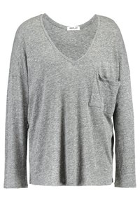 Graues Langarm-T-Shirt mit V-Ausschnitt, ausgestattet mit einer Brusttasche und Seitenschlitzen, aus einem weichen, strukturierten Material gefertigt. Markenlabel sichtbar.