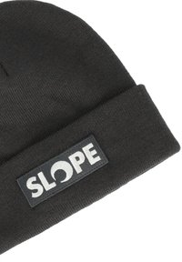 Mörkgrå stickad mössa med vikbar kant och en rektangulär svart lapp med vit text "SLOPE" och en cirkulär design.