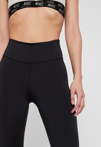 Czarne legginsy o wysokim stanie wykonane z elastycznego materiału o gładkiej fakturze. Posiadają szeroki pas z akcentem marki na górze.