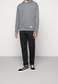 Felpa grigia con tasca frontale, abbinata a pantaloni neri e sneakers nere con dettagli bianchi. Tessuto liscio in tutto.