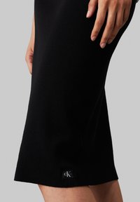 Abito in maglia nera con texture a costine, silhouette aderente e un piccolo tag con logo CK vicino all'orlo. Finitura liscia e design alla lunghezza del ginocchio.