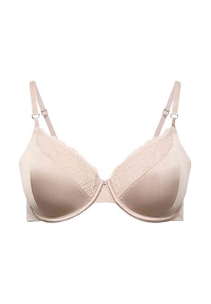 Mujer vista desde atrás abrochándose un sujetador beige claro, vistiendo bragas a juego con detalle de encaje, sobre un fondo liso y claro.