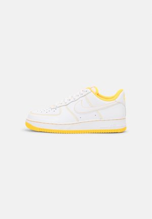 Weißer flacher Sneaker mit gelber Sohle, Futter und Naht, mit Perforationen und einem seitlichen Swoosh-Logo.