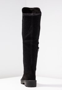 Schwarze Overknee-Stiefel mit einem glitzernden Textil-Obermaterial, einem unteren Abschnitt aus Wildleder und einer kontrastierenden klobigen Gummisohle mit einem seitlichen Reißverschluss.