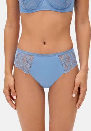 Mujer con conjunto de lencería de encaje azul claro, mostrando la zona media y la parte superior de los muslos sobre un fondo blanco liso.