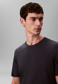 Dunkelgraues T-Shirt mit Rundhalsausschnitt aus weichem Stoff, mit kurzen Ärmeln und glatter Oberfläche, vor neutralem Hintergrund präsentiert.