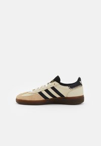 Sneakers met een crèmekleurige leren bovenkant, een ochre-suedetip, drie zwarte strepen, een zwarte hielkap en een getextureerde bruine rubberen zool.