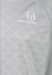 Lysegrå jakke med et geometrisk mønster og tekstureret stof. Inkluderer et hvidt logo af "Sergio Tacchini" på forsiden.