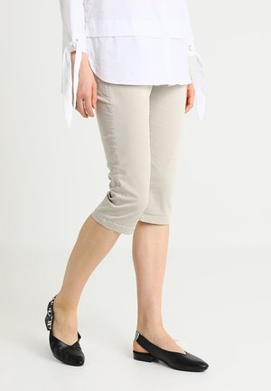 Pantaloni cropped beige chiaro con un design aderente e leggero stretch, abbinati a scarpe slingback nere con un accento a strisce.
