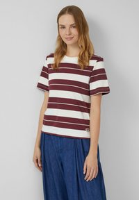 Gestreepte katoenen t-shirt in kastanjebruin en wit, ronde halslijn, korte mouwen, met een logo-detail op de zoom. Gecombineerd met losse blauwe broeken.