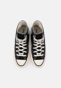 Schwarze High-Top-Sneaker aus Canvas mit weißen Schnürsenkeln, Gummispitzen und kontrastierenden Nähten. Strukturierter Stoff und klassisches Design.