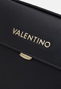 Černá kožená taška s texturou, zdobená zlatým logem "VALENTINO" a elegantním zlatým kováním pro zavírání.