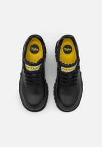 Sneaker in pelle nera con solette gialle, lacci tondi e suola tassellata. Presenta un'etichetta con il marchio "Buffalo" sulla linguetta.