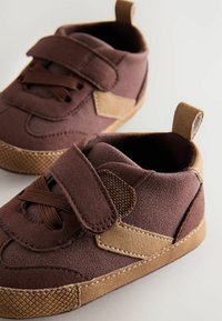 Chaussures pour enfants en suède marron avec une finition beige, de forme arrondie, équipées d'une bande auto-agrippante et de semelles en caoutchouc texturées, avec des détails de couture.