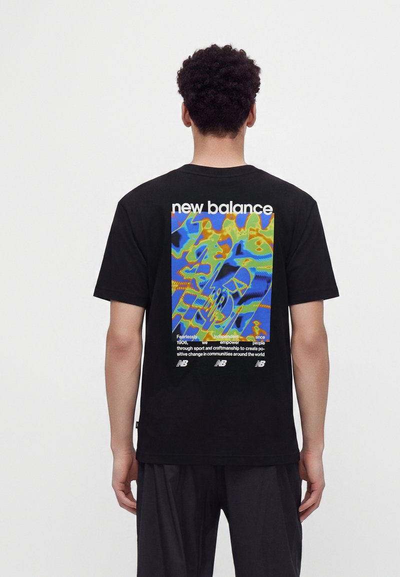 Άτομο με σγουρά μαλλιά που φοράει μαύρο T-shirt New Balance με πολύχρωμο αφηρημένο σχέδιο και κείμενο στην πλάτη.