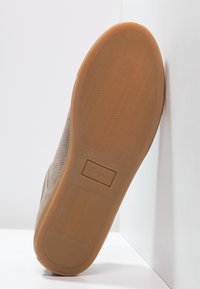 Bruna mockaskor med en texturerad beigefärgad gummisula som har ett vågigt mönster och en liten logotyp på sidan.