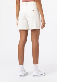 Shorts bianchi in cotone con tasche posteriori, taglio dritto e una sottile etichetta con logo. Indossati con sneakers bianche e calze corte.