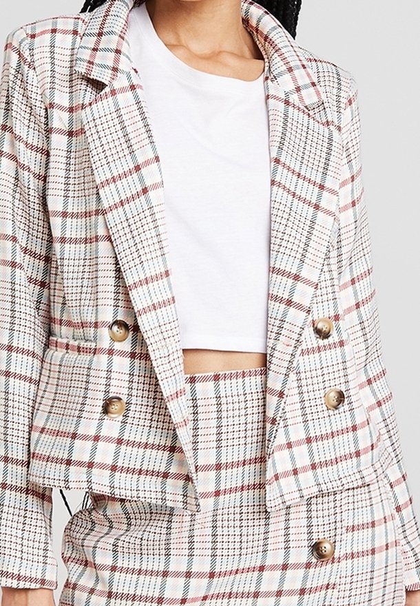 Femme portant un crop top blanc sous un blazer à carreaux beige, rouge et noir à double boutonnage ainsi qu'une jupe taille haute assortie.