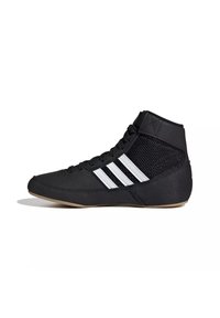 Chaussure de sport noire montante avec trois bandes blanches, panneaux latéraux en mesh, lacets noirs et semelle marron clair, vue de profil.