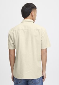 Korte mouwen shirt in off-white stof, met een ontspannen pasvorm, kraag en achterkant met een yoke-detail, gecombineerd met blauwe denim jeans.