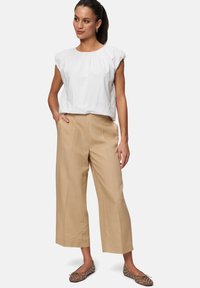 Haut blanc à manches courtes avec des détails froncés, associé à un pantalon large beige. Ballerines marron avec des accents cloutés. Silhouette simple et structurée.