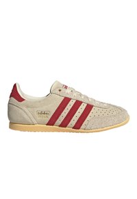 Baskets Adidas Japan beige avec des bandes rouges, empeigne en suède perforé, semelle en gomme et marquage doré « adidas JAPAN » sur le côté.