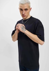 Svart oversized t-skjorte laget av mykt stoff, med korte ermer og rund hals, kombinert med mørk denim jeans. Enkel design.