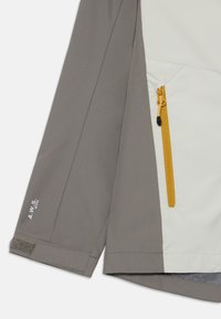 Veste légère bicolore avec une palette de couleurs gris et blanc cassé, poche zippée avec fermeture éclair jaune et détails en tissu.